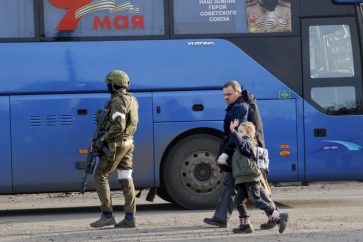 Des civils évacués d'Azovstal marchent vers un bus escorté par des militaires russes à Marioupol, le 6 mai 2022.